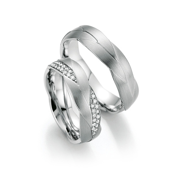 Zwei silberne Ringe, einer verziert mit einer Reihe kleiner Diamanten, gefasst auf weißem Grund - zeitlose Eleganz aus dem Hochzeitshaus Konstanz.