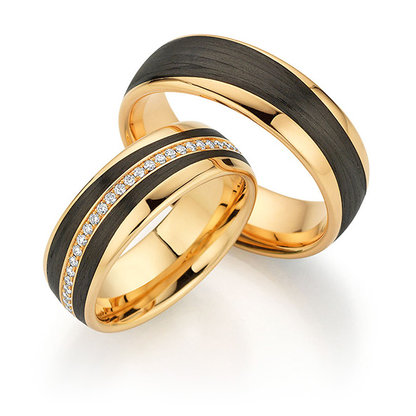 Zwei Goldringe mit schwarzen Bändern, einer davon mit einer Reihe kleiner Diamanten in der Mitte - perfekt für Paare, die im Hochzeitshaus in Konstanz einkaufen, wo Eleganz auf zeitloses Design trifft.
