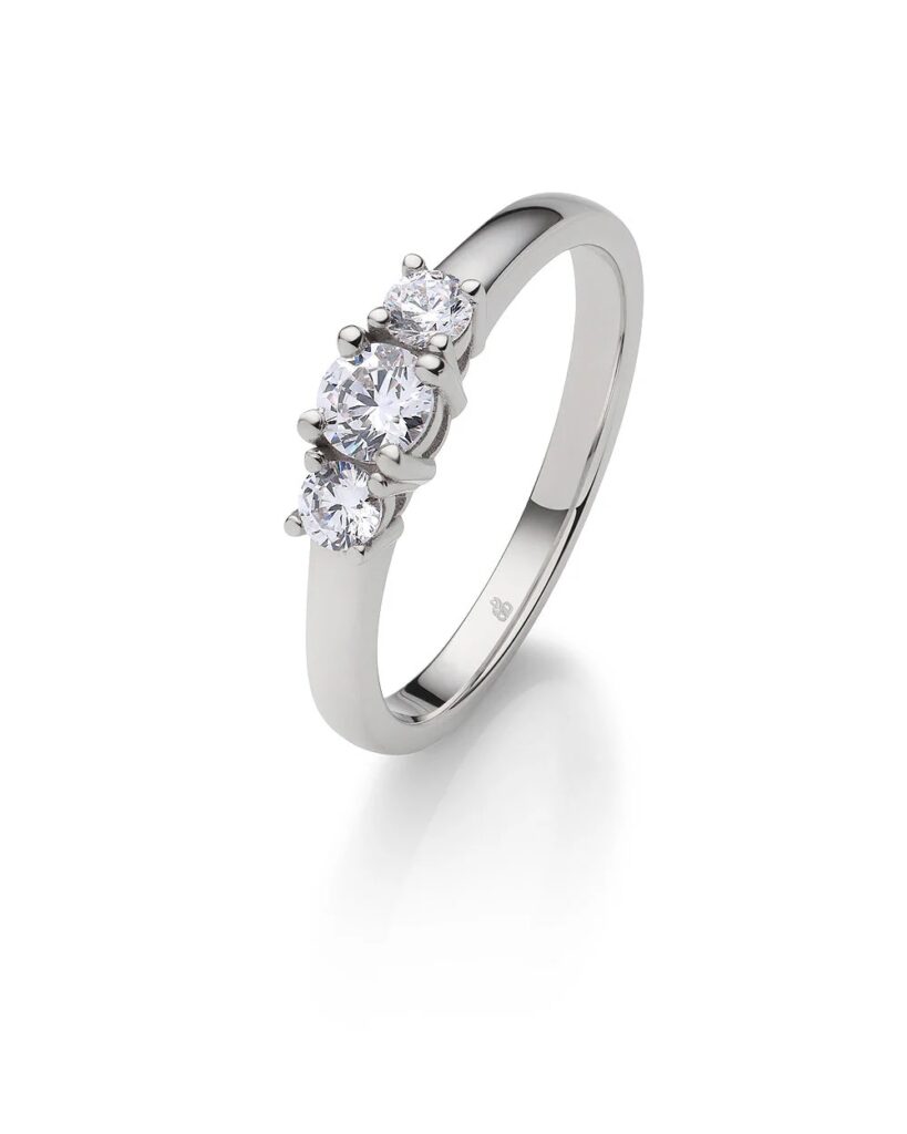 Ein Ring aus Weißgold mit drei runden, funkelnden Diamanten in einer Reihe auf einem schlichten Band - eine elegante Wahl, die im Hochzeitshaus Konstanz gefunden wurde, das für exquisiten Schmuck und Herrenanzüge bekannt ist.