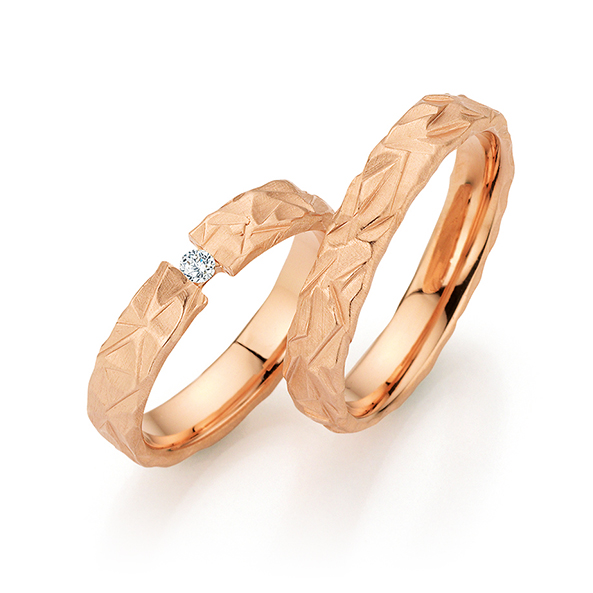 Zwei roségoldene Ringe mit strukturiertem, geometrischem Muster, einer davon mit kleinem Diamant-Akzent - perfekt zur Ergänzung von moderner Brautmode und stilvollen Herrenanzügen.