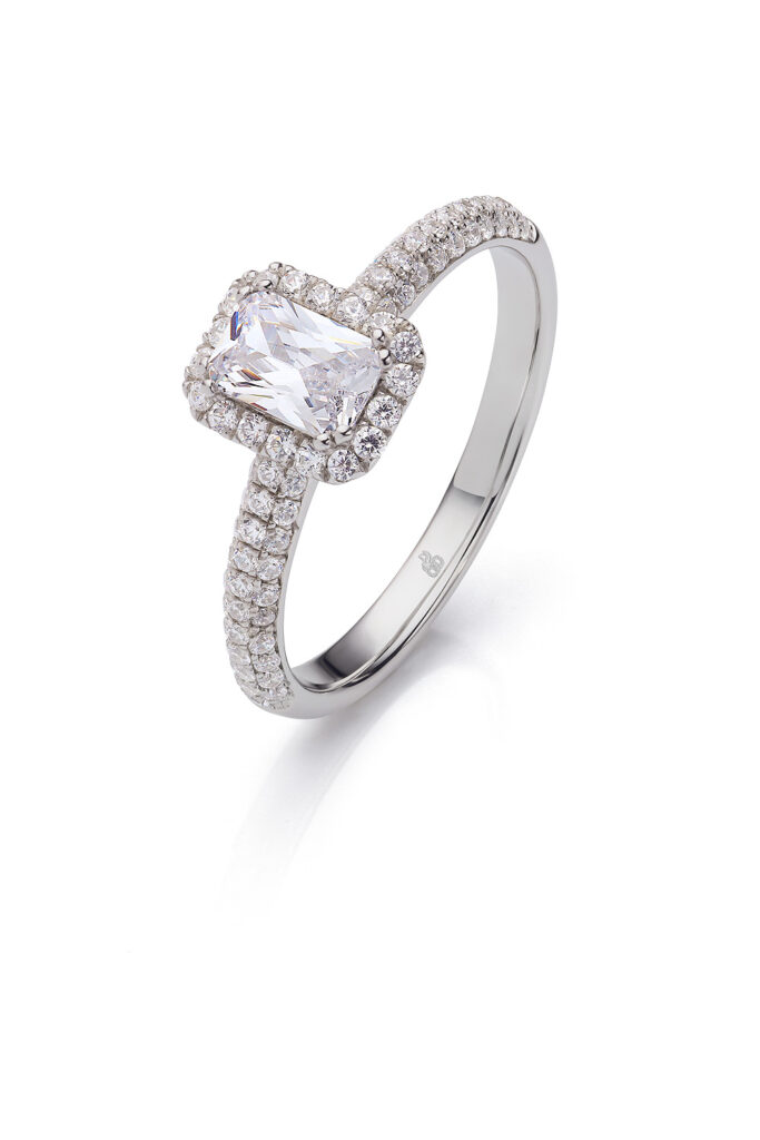 Verlobungsring mit Diamant im Radiant-Schliff, der sich durch ein automatisches Design mit Halo und einem mit Pavé-Fassung verzierten Ringband auszeichnet.