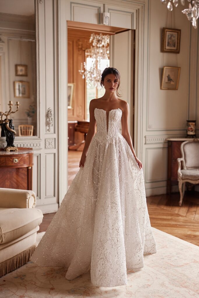 Eine Frau in einem trägerlosen weißen Brautkleid steht in einem eleganten Raum im Vintage-Stil mit kunstvoller Ausstattung.